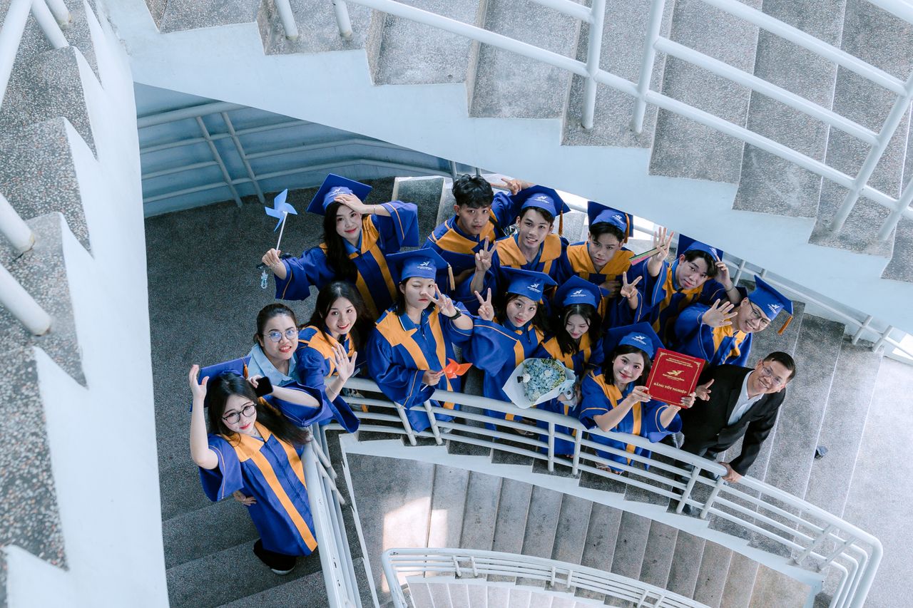 ours-journey Cheerful graduates in blue gowns celebrate on a spiral staircase, capturing a joyous moment.