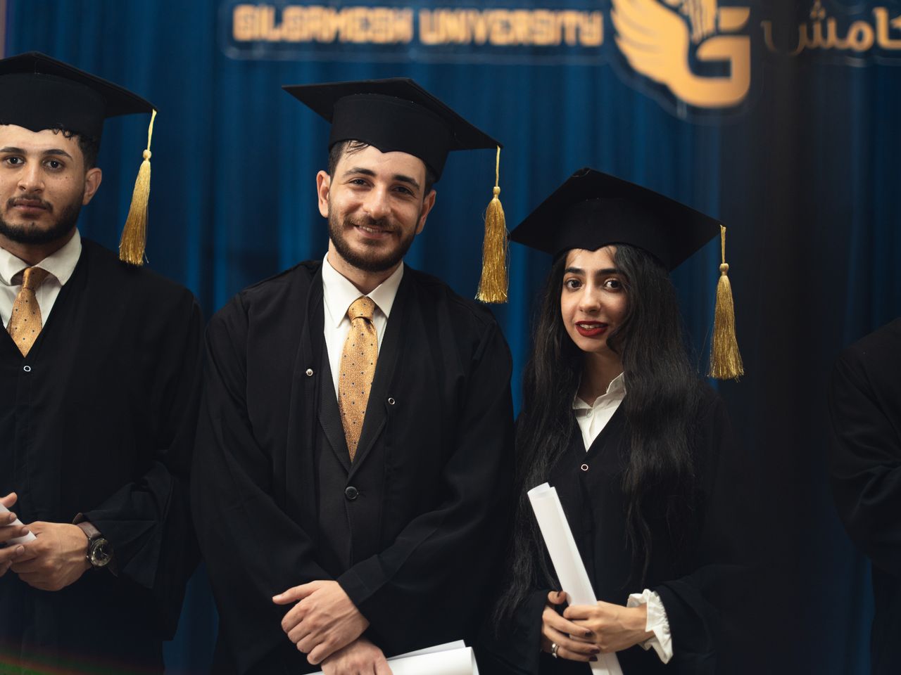 about-img Smiling graduates holding diplomas at Gilgamesh University ceremony.