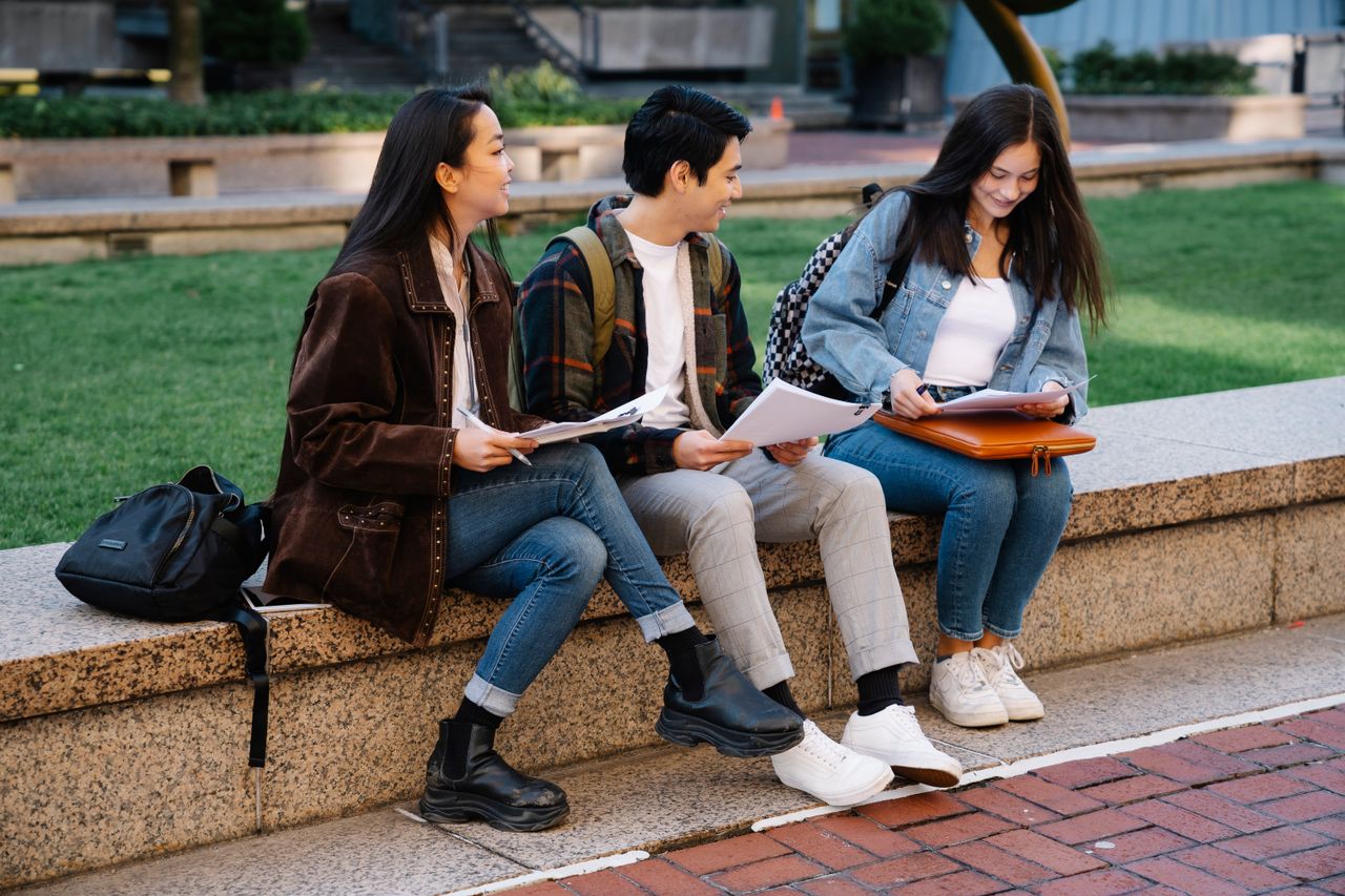Crafting Captivating Headlines: Your awesome post title goes here Three college students engaged in study session on a campus bench, enjoying a sunny day.